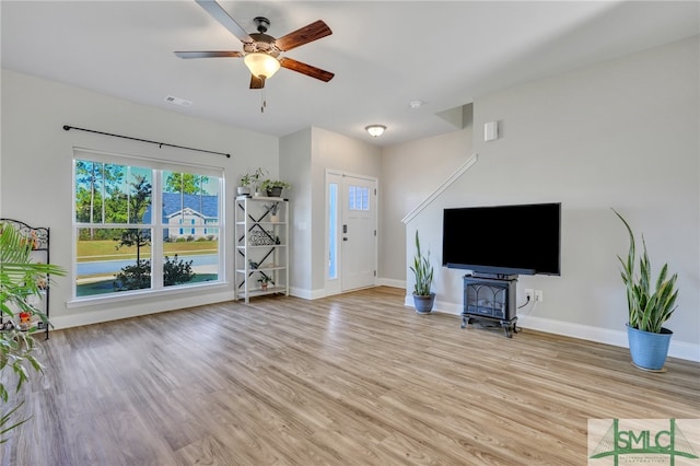 unfurnished living room featuring ceiling fan, light hardwood / wood-style floors, and a wood stove