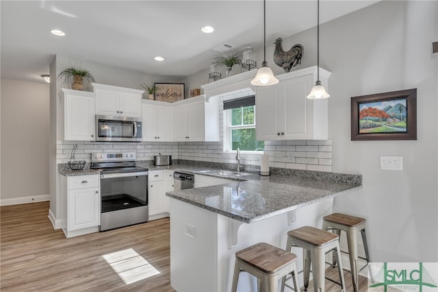 kitchen featuring kitchen peninsula, sink, decorative light fixtures, white cabinetry, and appliances with stainless steel finishes