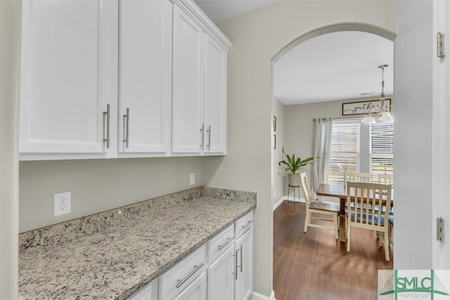 kitchen featuring light stone countertops, dark wood-type flooring, white cabinetry, and hanging light fixtures