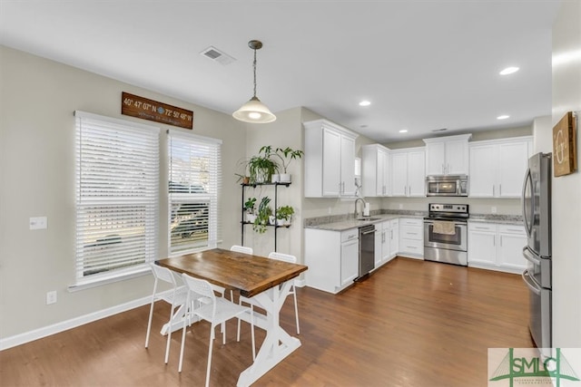 kitchen with white cabinets, pendant lighting, appliances with stainless steel finishes, light stone counters, and dark hardwood / wood-style flooring