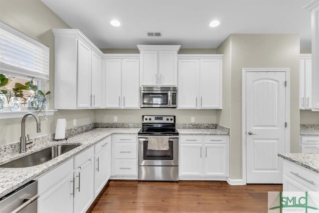 kitchen featuring dark wood-type flooring, sink, light stone countertops, white cabinetry, and appliances with stainless steel finishes