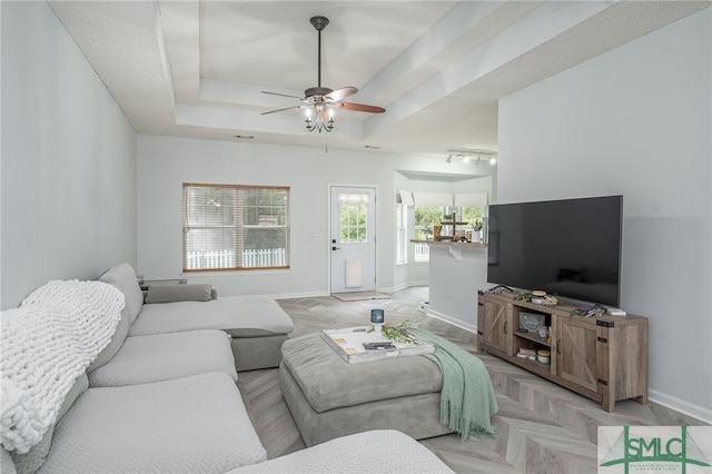 living room with a ceiling fan, a tray ceiling, and baseboards