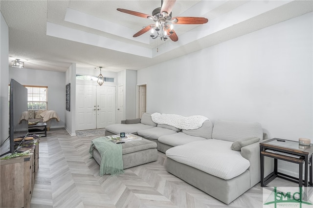 living room with a textured ceiling, ceiling fan, a tray ceiling, and light parquet floors