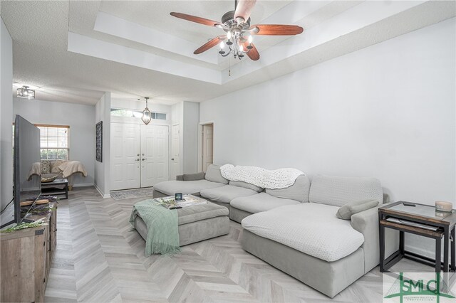 living room featuring a ceiling fan, a raised ceiling, and baseboards