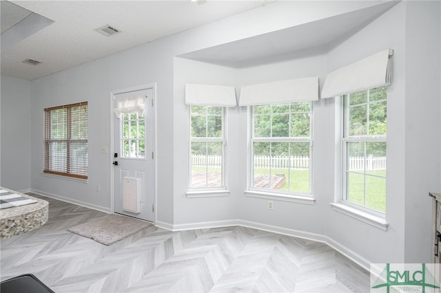 doorway to outside featuring a textured ceiling, a healthy amount of sunlight, and light parquet floors