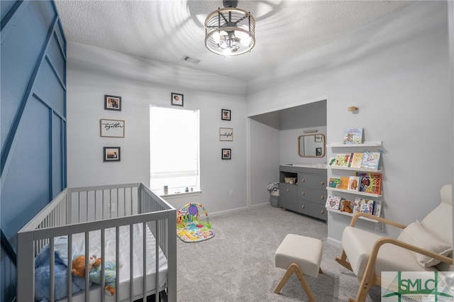 bedroom featuring a crib, carpet flooring, baseboards, visible vents, and a textured ceiling