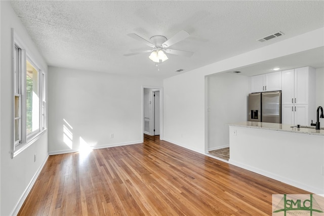 unfurnished living room featuring light hardwood / wood-style flooring, a textured ceiling, sink, and ceiling fan