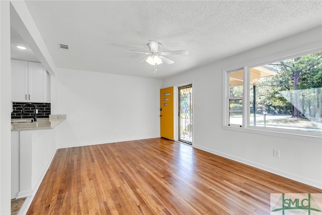 unfurnished living room featuring sink, light hardwood / wood-style flooring, a textured ceiling, and ceiling fan