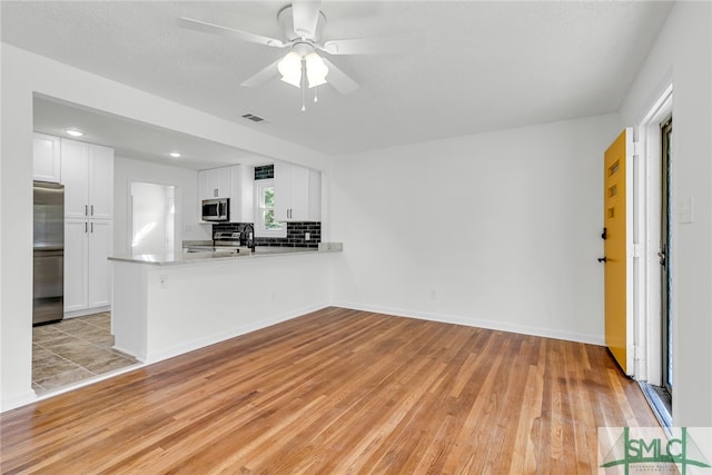 kitchen featuring decorative backsplash, kitchen peninsula, white cabinets, light wood-type flooring, and appliances with stainless steel finishes