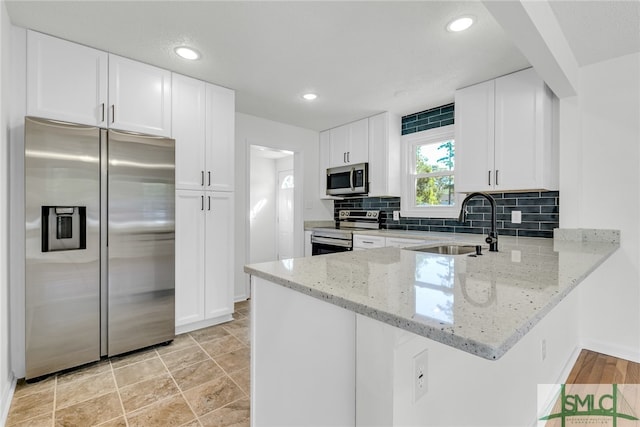 kitchen featuring appliances with stainless steel finishes, white cabinets, light stone counters, and sink