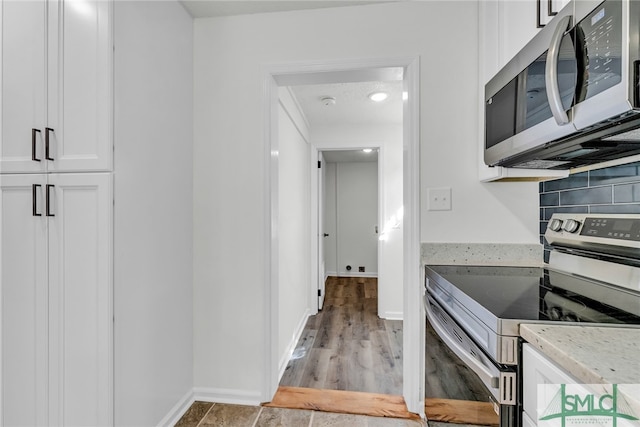 kitchen featuring white cabinets, backsplash, appliances with stainless steel finishes, light hardwood / wood-style floors, and light stone counters