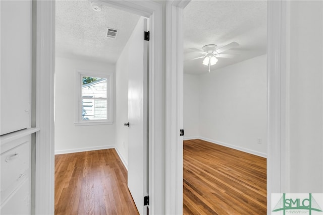 hallway with a textured ceiling and wood-type flooring