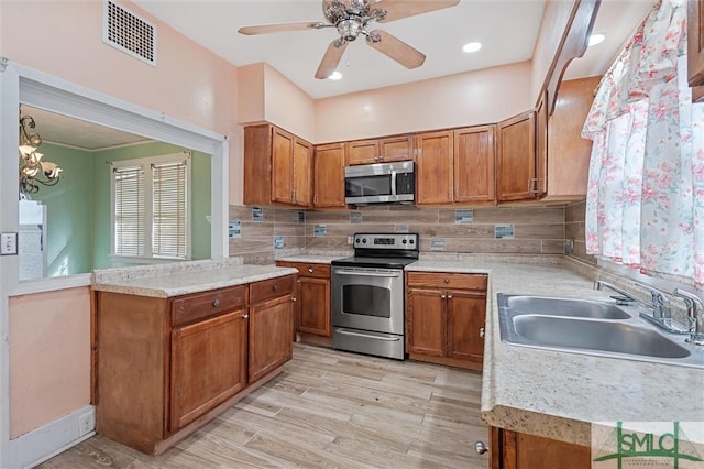 kitchen with sink, light hardwood / wood-style flooring, decorative backsplash, ceiling fan with notable chandelier, and appliances with stainless steel finishes