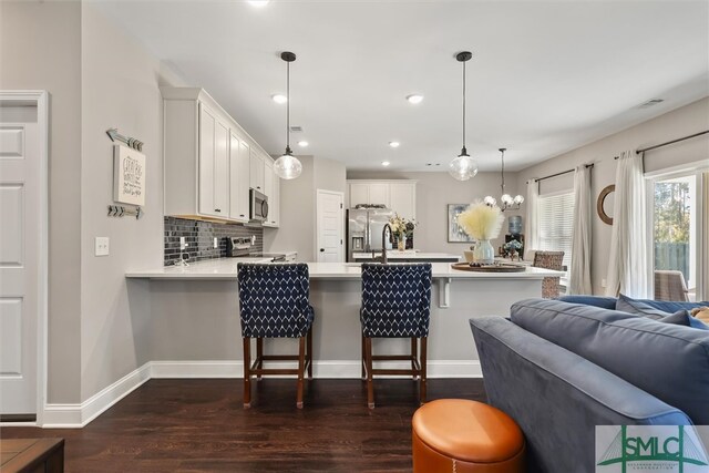 kitchen with kitchen peninsula, white cabinets, appliances with stainless steel finishes, a kitchen bar, and decorative light fixtures