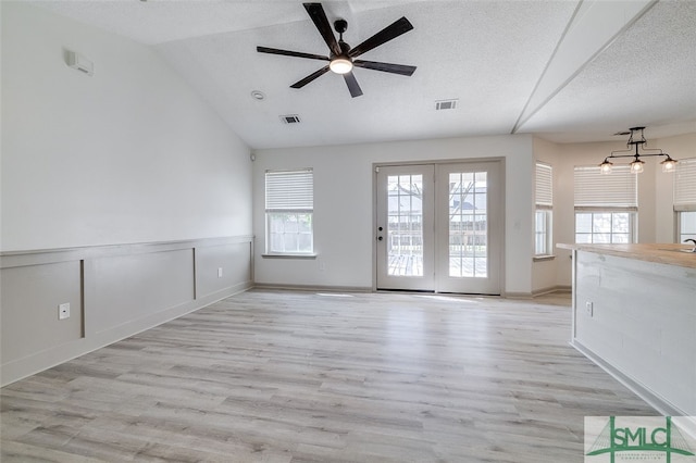 unfurnished living room featuring light hardwood / wood-style floors, lofted ceiling, a textured ceiling, and ceiling fan