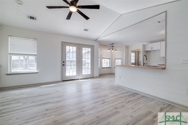 unfurnished living room with light wood-type flooring, a textured ceiling, vaulted ceiling, and plenty of natural light