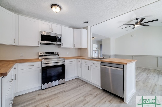 kitchen featuring kitchen peninsula, white cabinetry, wooden counters, and stainless steel appliances