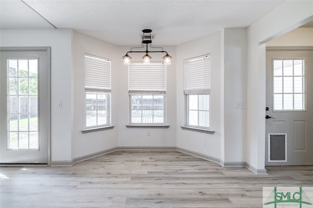 unfurnished dining area featuring light hardwood / wood-style flooring, a textured ceiling, and plenty of natural light