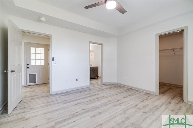 unfurnished bedroom featuring connected bathroom, a closet, light hardwood / wood-style flooring, a walk in closet, and ceiling fan