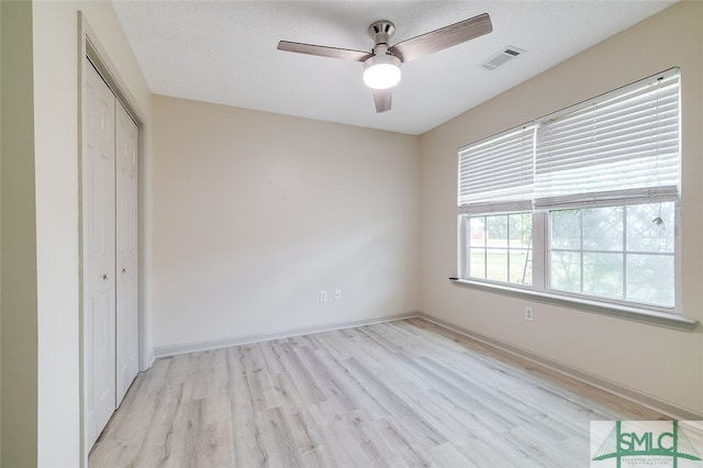 unfurnished bedroom featuring light hardwood / wood-style flooring, a closet, a textured ceiling, and ceiling fan