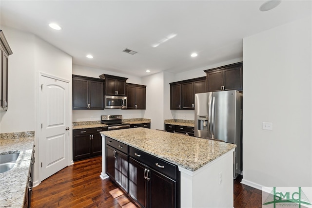 kitchen featuring a kitchen island, dark wood-type flooring, stainless steel appliances, dark brown cabinets, and light stone counters