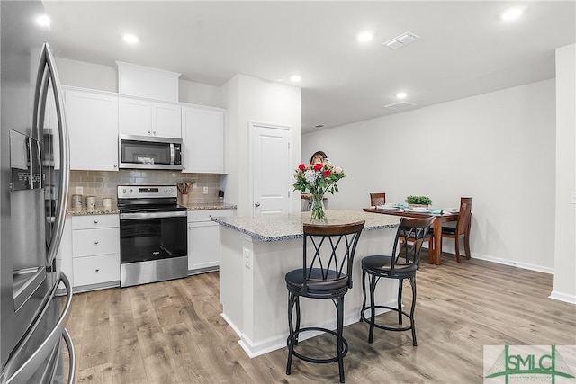 kitchen featuring a kitchen island, light stone countertops, light wood-type flooring, white cabinetry, and appliances with stainless steel finishes