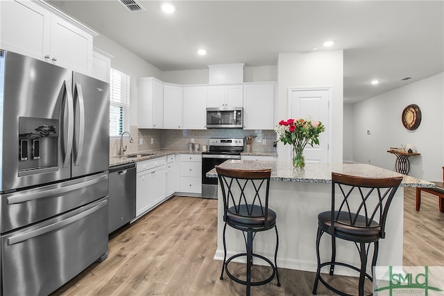 kitchen featuring white cabinets, a kitchen island, appliances with stainless steel finishes, light stone countertops, and sink