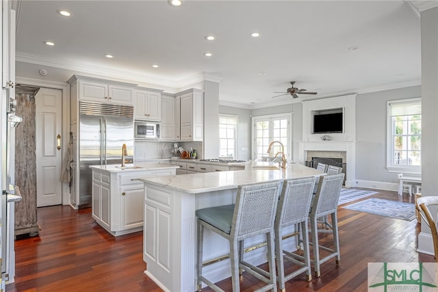 kitchen with a center island with sink, built in appliances, a kitchen bar, and dark hardwood / wood-style flooring