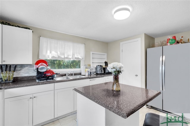 kitchen with sink, a textured ceiling, a center island, white cabinetry, and white fridge