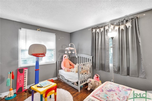 bedroom featuring dark hardwood / wood-style floors, a crib, and a textured ceiling