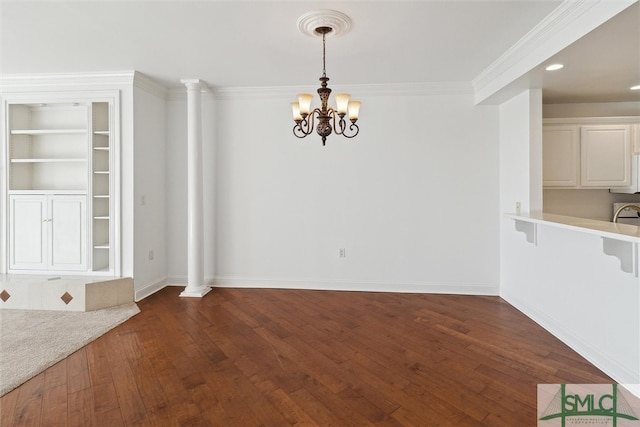 unfurnished dining area featuring dark hardwood / wood-style floors, decorative columns, crown molding, an inviting chandelier, and built in shelves