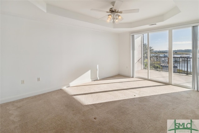 carpeted empty room featuring a tray ceiling, a water view, and ceiling fan