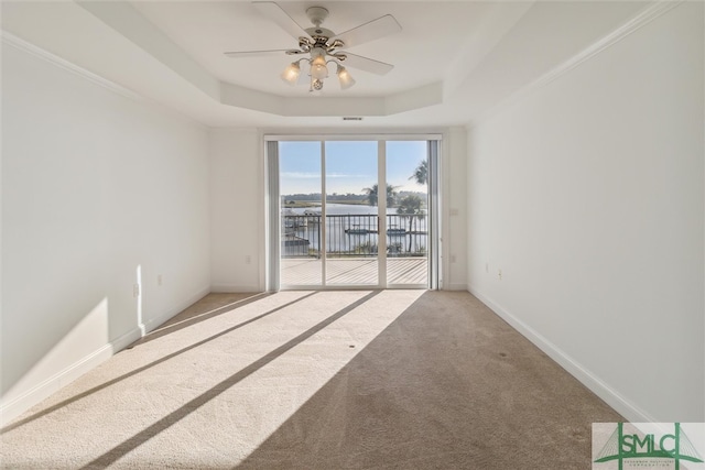 carpeted spare room with crown molding, ceiling fan, a water view, and a raised ceiling