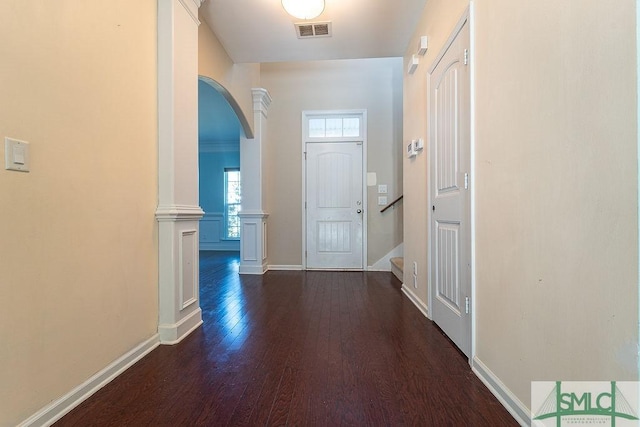 hallway with arched walkways, dark wood finished floors, decorative columns, visible vents, and baseboards