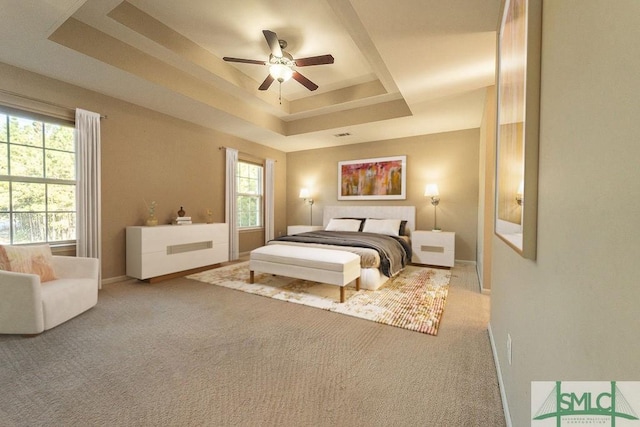 carpeted bedroom featuring baseboards, a tray ceiling, and a ceiling fan