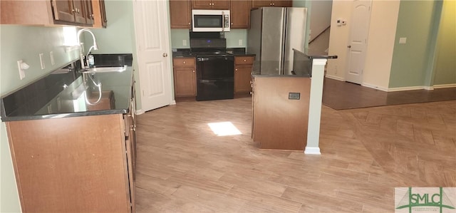 kitchen with dark countertops, appliances with stainless steel finishes, a sink, light wood-type flooring, and baseboards