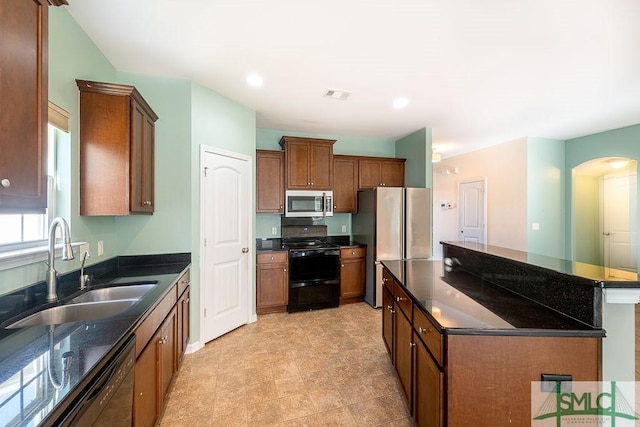 kitchen featuring arched walkways, a kitchen island, brown cabinets, black appliances, and a sink