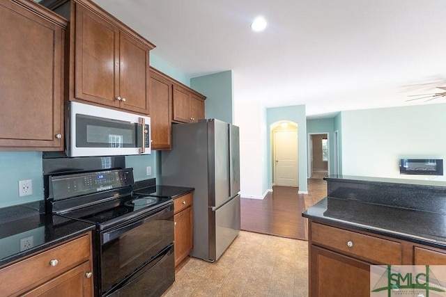 kitchen featuring stainless steel appliances, dark stone counters, brown cabinetry, and ceiling fan