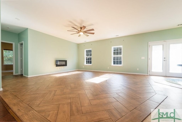 unfurnished living room featuring a healthy amount of sunlight, baseboards, french doors, and a glass covered fireplace