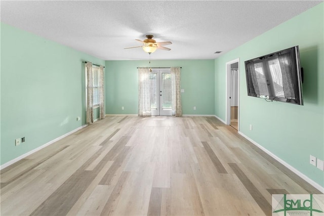 unfurnished room featuring light wood-style flooring, french doors, a textured ceiling, and baseboards