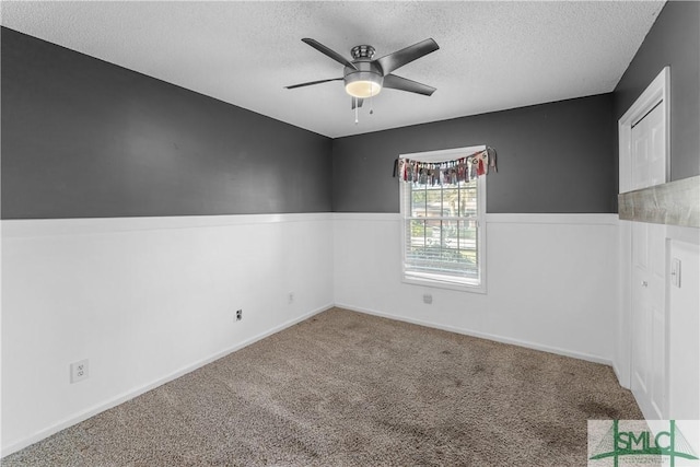 unfurnished room with wainscoting, ceiling fan, a textured ceiling, and carpet