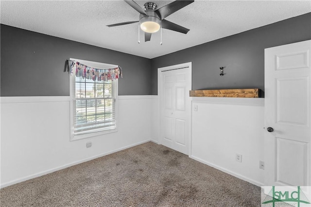 unfurnished bedroom featuring a ceiling fan, a wainscoted wall, a closet, a textured ceiling, and carpet flooring