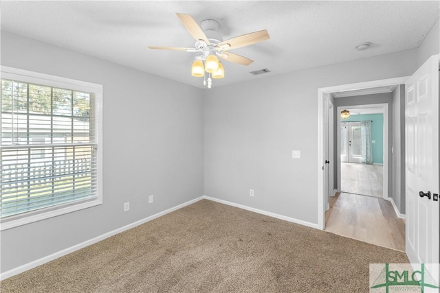 unfurnished bedroom featuring visible vents, light carpet, baseboards, and ceiling fan