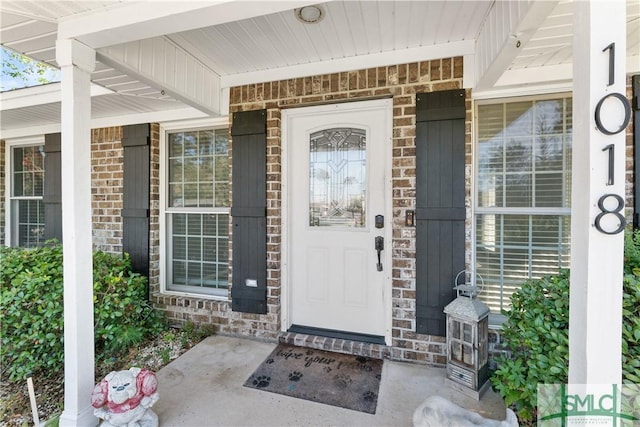 view of exterior entry with brick siding and covered porch