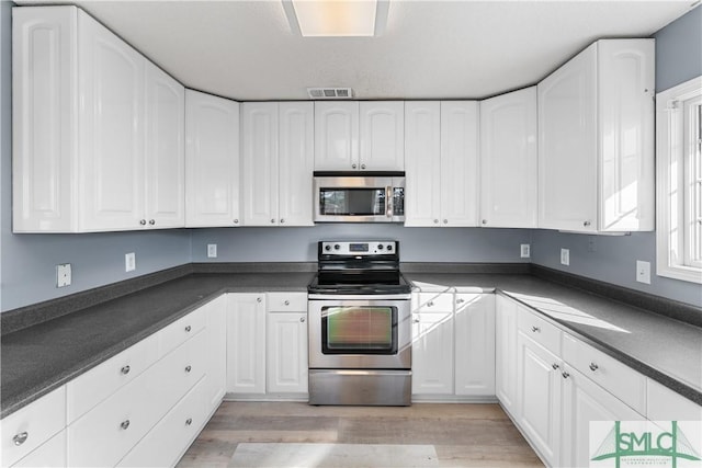 kitchen with dark countertops, white cabinets, visible vents, and appliances with stainless steel finishes