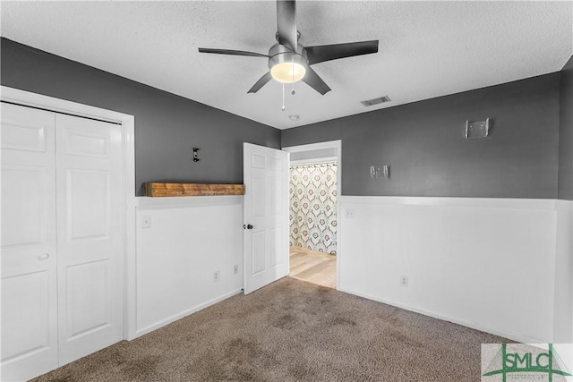 empty room featuring carpet flooring, visible vents, a textured ceiling, and ceiling fan