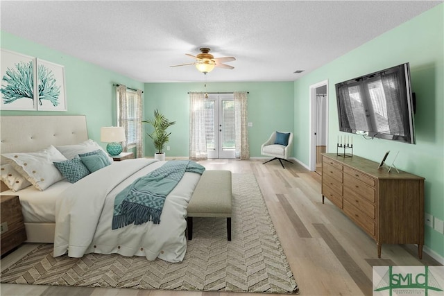 bedroom featuring french doors, baseboards, a textured ceiling, and light wood finished floors