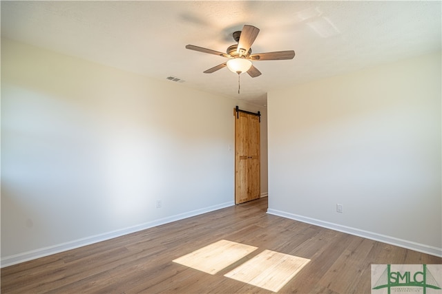 spare room with a barn door, light hardwood / wood-style flooring, and ceiling fan