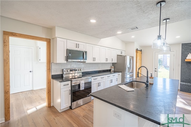 kitchen with white cabinets, a barn door, sink, decorative light fixtures, and stainless steel appliances