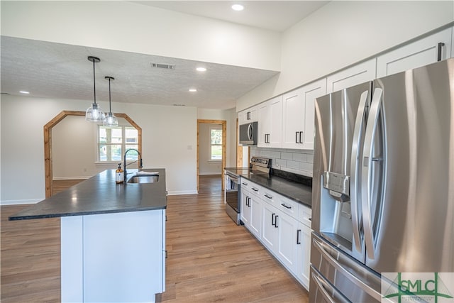 kitchen featuring sink, appliances with stainless steel finishes, white cabinets, and an island with sink